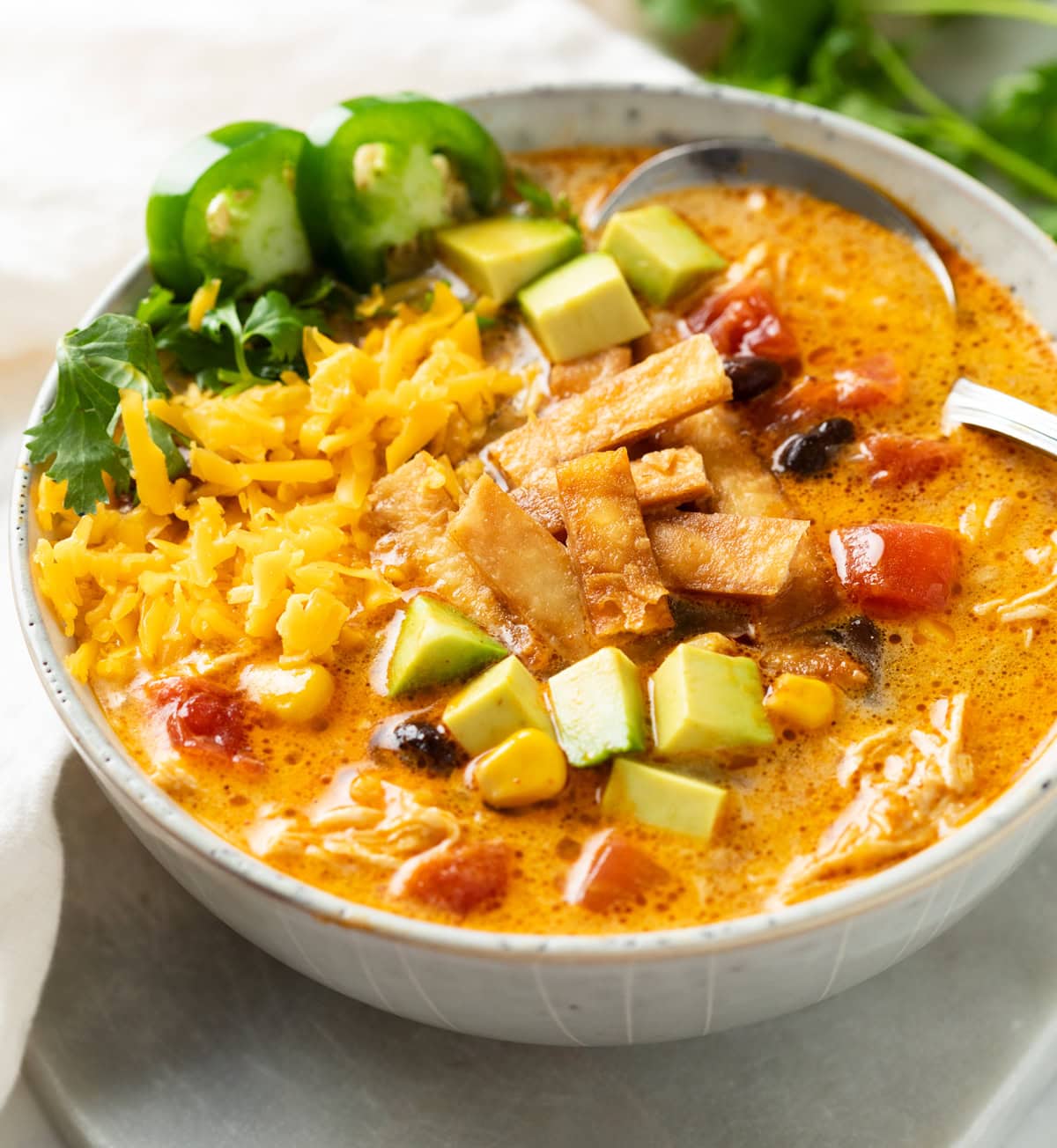 Chicken Tortilla Soup in a soup bowl with colorful toppings and a spoon in the back.