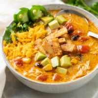 A bowl of Creamy Chicken Tortilla Soup topped with crispy tortillas, diced avocado, shredded cheese, jalapenos, and cilantro.