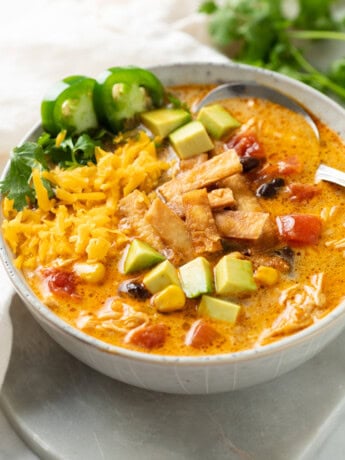 A bowl of Creamy Chicken Tortilla Soup topped with crispy tortillas, diced avocado, shredded cheese, jalapenos, and cilantro.