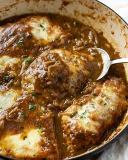 A skillet of French Onion Chicken in a dark sauce with caramelized onions and melted cheese.