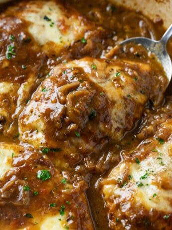 A spoon scooping up French Onion Chicken from a skillet with melted cheese on top.