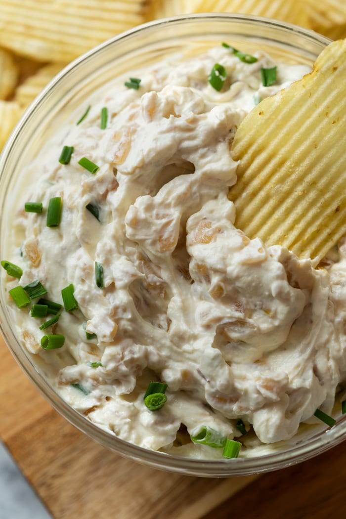 A glass bowl full of French Onion Dip topped with chives and a Ruffled Chip.