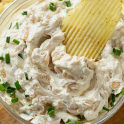 A ruffled Chip dipped into French Onion Dip with chives on top.