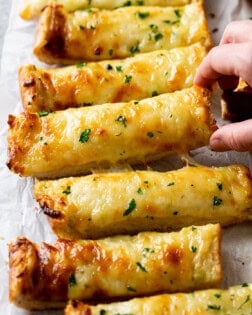 A hand picking up Garlic Bread with Cheese.