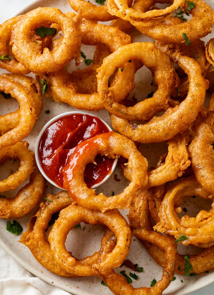 Onion Rings piled up on a plate with a ramekin of ketchup.