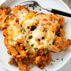 A scoop of cheesy baked pasta on a white plate with a fork.