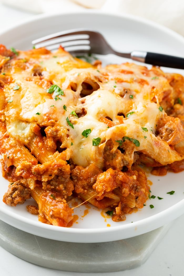 A white plate with Cheesy Pasta Bake with meat and a fork in the background.