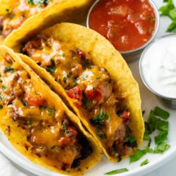 Baked Tacos on a white plate next to salsa and sour cream.