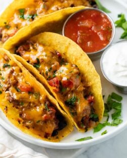 Baked Tacos on a white plate next to salsa and sour cream.