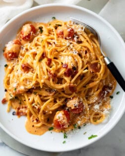 A white plate with creamy bacon pasta on it with spaghetti and crispy bacon.