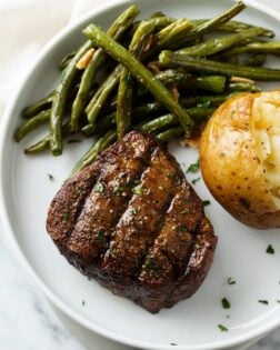 A filet mignon with steak rub on top next to roasted green beans and a baked potato.