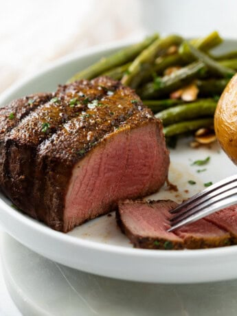 A medium rare filet mignon with a slice cut into it and green beans in the background.