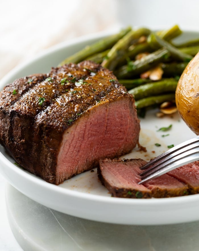 A medium rare filet mignon with a slice cut into it and green beans in the background.
