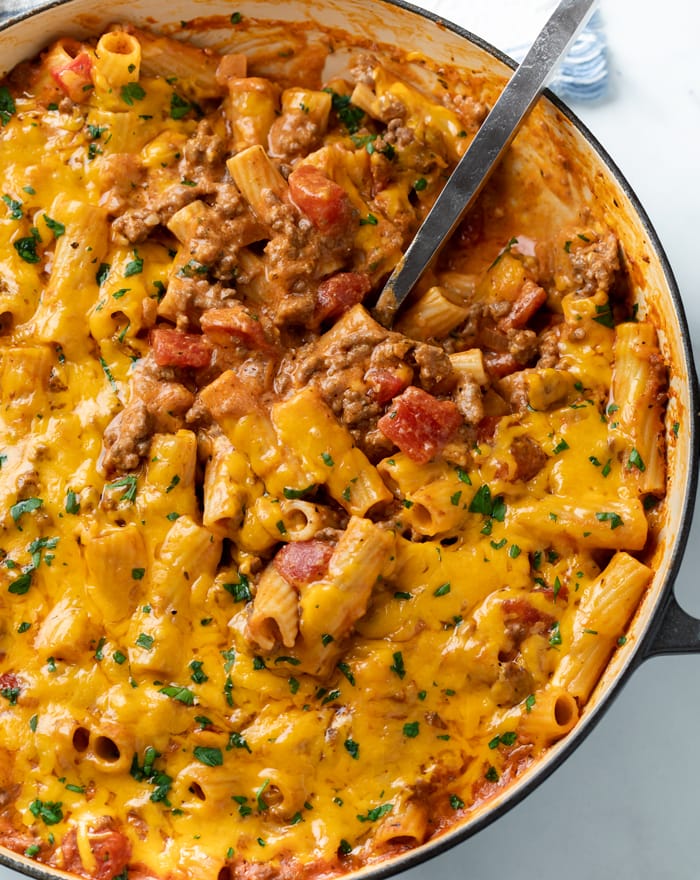 A casserole dish filled with ground beef casserole with a spoon in it and melted cheese on top.