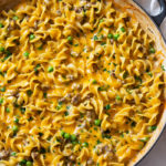 A skillet filled with ground beef stroganoff in a creamy sauce with peas and egg noodles.