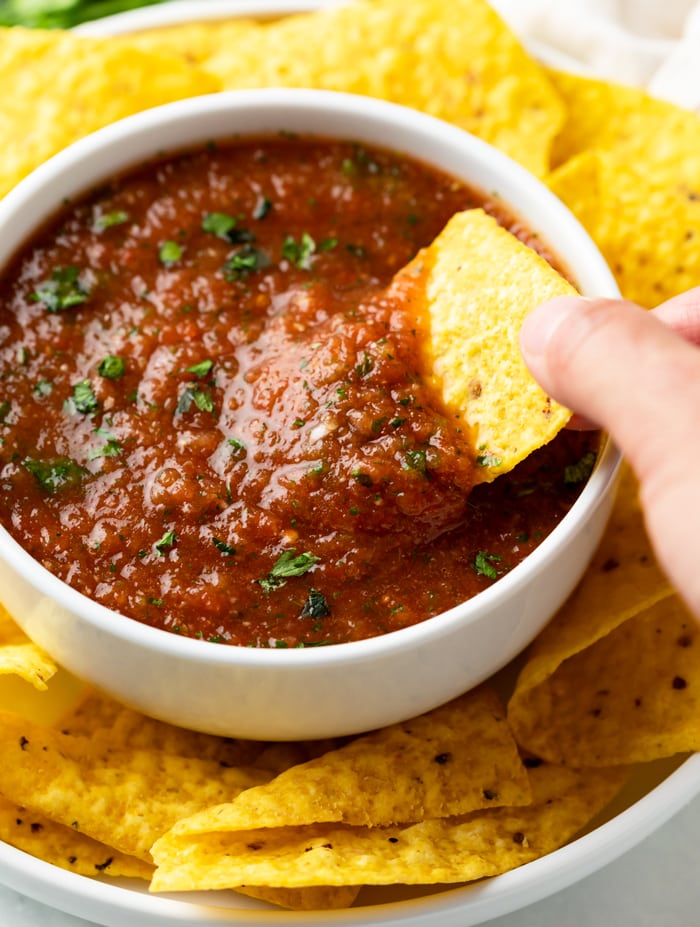 A white bow full of salsa with a tortilla chip being dipped into it.