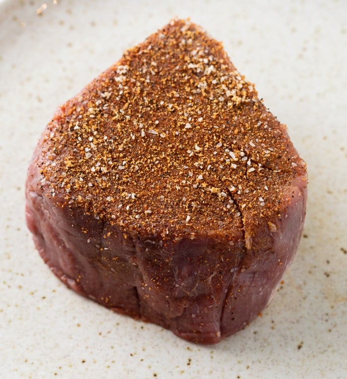 Uncooked filet mignon with steak seasoning on top.
