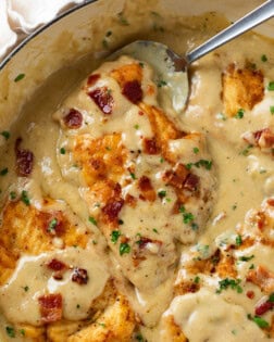 A skillet with Smothered Chicken in gravy topped with crispy bacon and parsley.