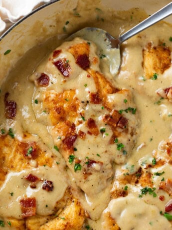 A skillet with Smothered Chicken in gravy topped with crispy bacon and parsley.