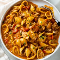 Taco Pasta with shells on a white plate in a creamy red sauce with tomatoes.