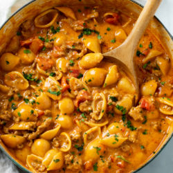 A pot filled with creamy, cheesy, Taco Pasta with a wooden spoon and parsley on top.