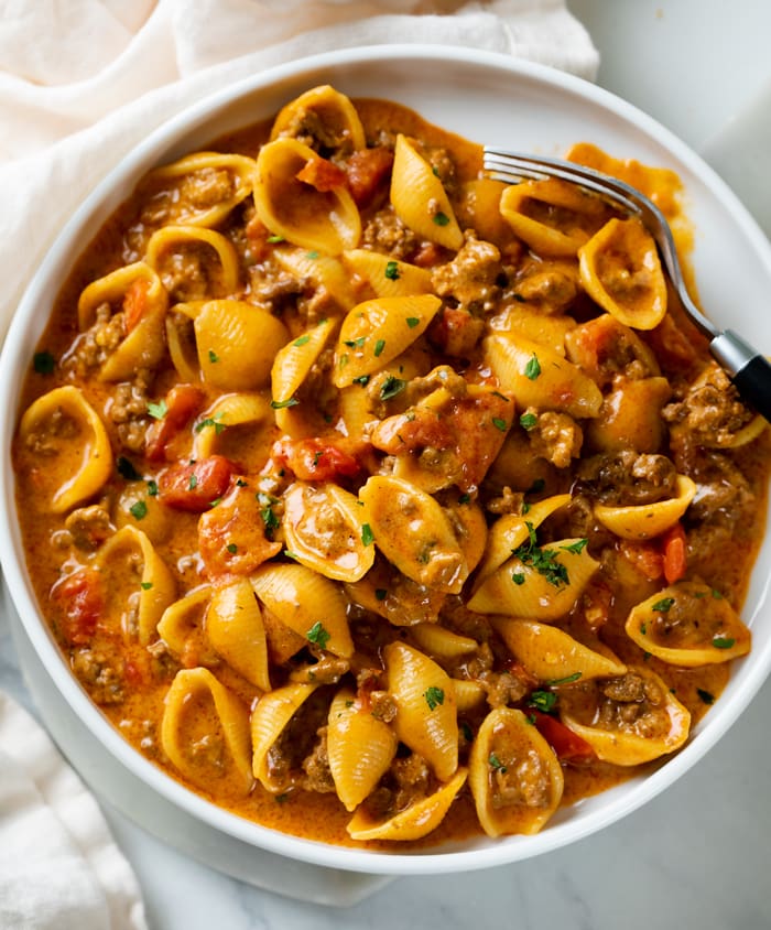 Taco Pasta with shells on a white plate in a creamy red sauce with tomatoes.