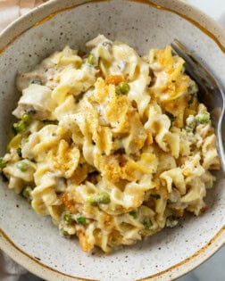 A bowl of Tuna Noodle Casserole with egg noodles in cream sauce with peas and crushed Ritz on top.