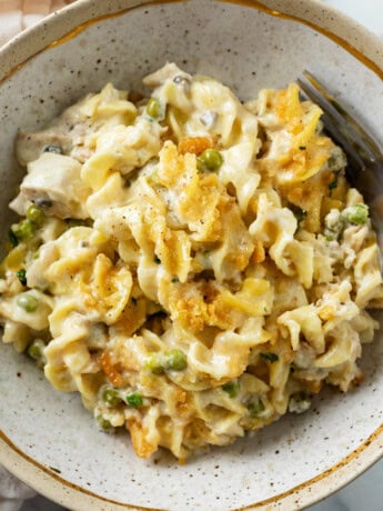 A bowl of Tuna Noodle Casserole with egg noodles in cream sauce with peas and crushed Ritz on top.