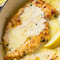 A skillet filled with Creamy Lemon Chicken with freshly sliced lemon wedges and parsley.