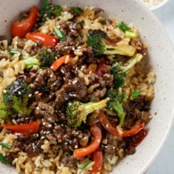 A bowl of rice with Ground Beef with Broccoli on top with bell peppers and green onions.
