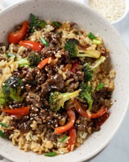 A bowl of rice with Ground Beef with Broccoli on top with bell peppers and green onions.