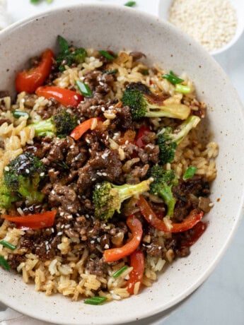 A bowl of rice with Ground Beef with Broccoli on top with bell peppers and green onions.