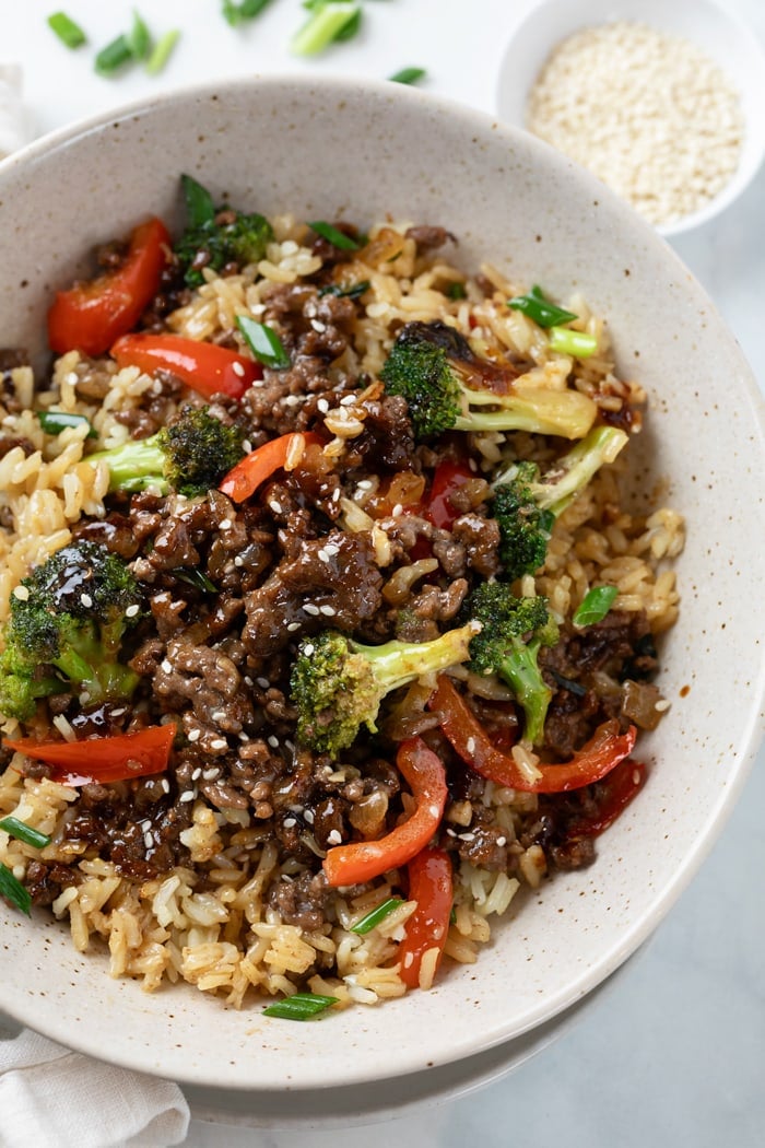 A bowl of rice with Ground Beef with Broccoli on top with bell peppers and green onions.