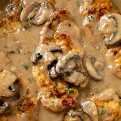 A skillet with Mushroom Chicken covered in a creamy sauce with mushrooms and parsley.