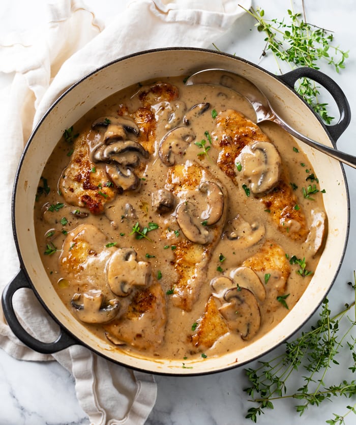 A pot with mushroom chicken in a creamy sauce with thyme on the side.