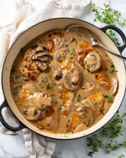 A pot with mushroom chicken in a creamy sauce with thyme on the side.