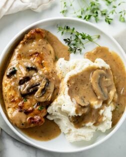 A white plate with mushroom chicken and mashed potatoes topped with Creamy Sauce.