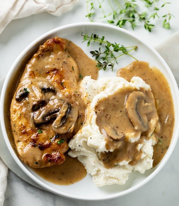 A white plate with mushroom chicken and mashed potatoes topped with Creamy Sauce.