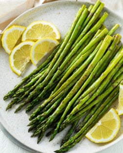 A white plate with roasted asparagus on top with sliced lemons.