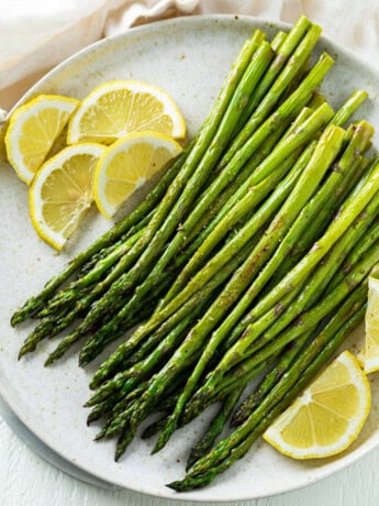 A white plate with roasted asparagus on top with sliced lemons.