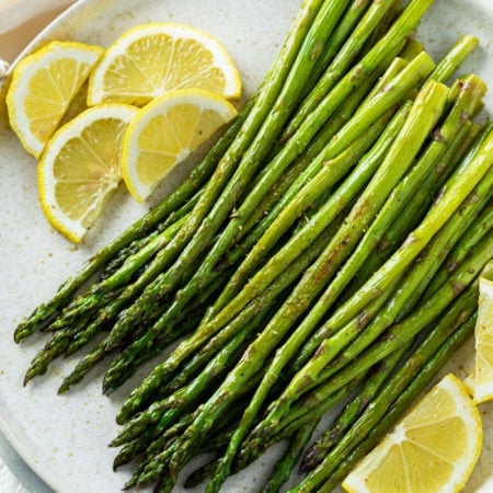 A white plate with roasted asparagus on top with sliced lemons.