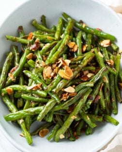 A white bowl filled with roasted green beans with thinly sliced almonds on top.