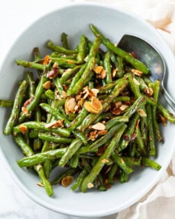 A white bowl with roasted green beans and almonds with a spoon on the side.