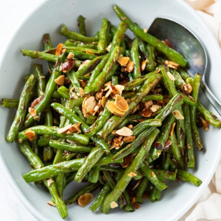 A white bowl with roasted green beans and almonds with a spoon on the side.