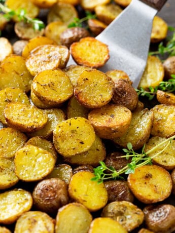 A spatula scooping crispy roasted potatoes from a baking sheet.