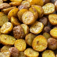 Roasted potatoes on a baking sheet with crispy skin and seasonings.