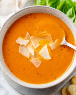 A bowl with Tomato Soup topped with shaved Parmesan Cheese with a spoon.