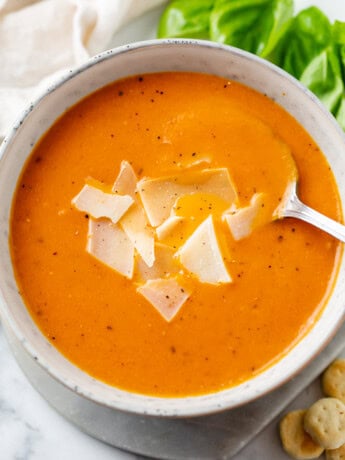 A bowl with Tomato Soup topped with shaved Parmesan Cheese with a spoon.