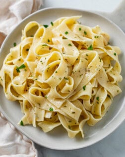 A white plate with buttered noodles topped with herbs.