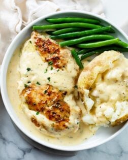 A white plate with Creamy Ranch Chicken next to a baked potato and green beans.